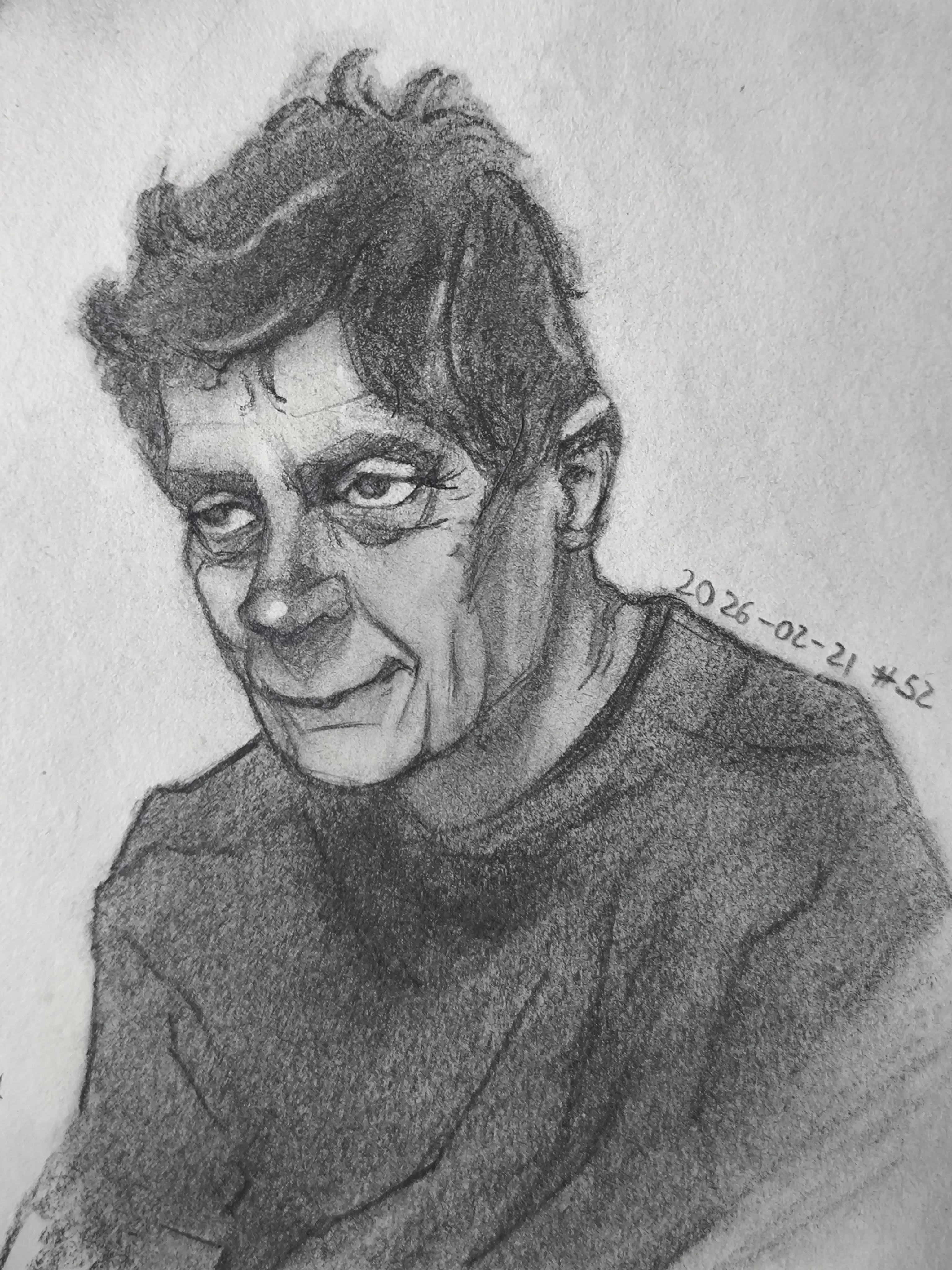 Graphite portrait sketch of a man with messy dark hair, heavy shaded eye sockets, and a slight smirk. He is turned a bit to the side, wearing a dark sweater, with soft smudged shading.