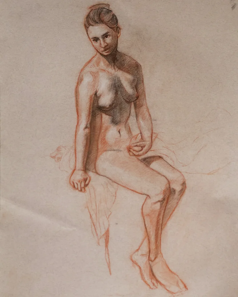 Seated nude figure study of a woman, drawn with red and dark pencil. She sits on edge with one hand resting, body slightly turned, soft shading on torso and legs.